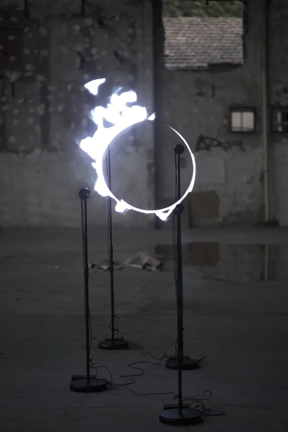 Dans une friche industrielle aux murs de béton, quatre hélices sur pied dessinent dans l'air un anneau blanc incandescent, comme une éclipse.